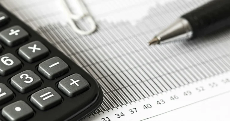 Foto em preto e branco de uma calculadora e uma caneta em cima de uma folha de papel com números para ilustrar o tema Imposto de Transmissão Causa Mortis, conhecido por ITCMD, o que é e como é calculado