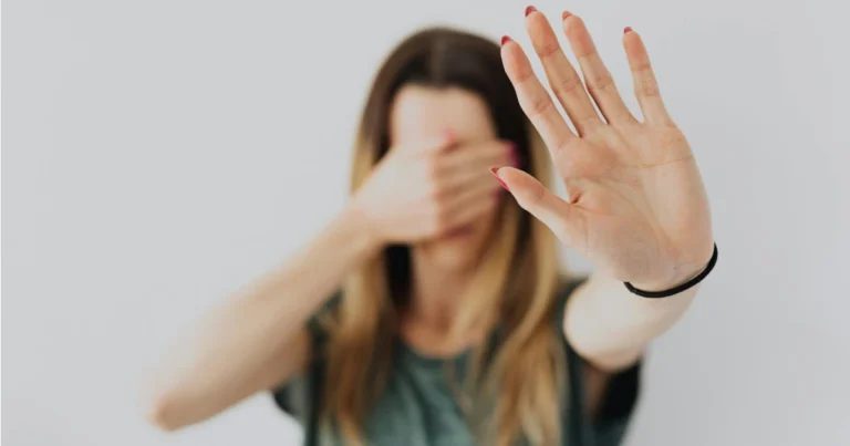 Mulher cobrindo o rosto com a mão direita e estendo a mãe esqueda aberta representando a violência doméstica e medidas de proteção