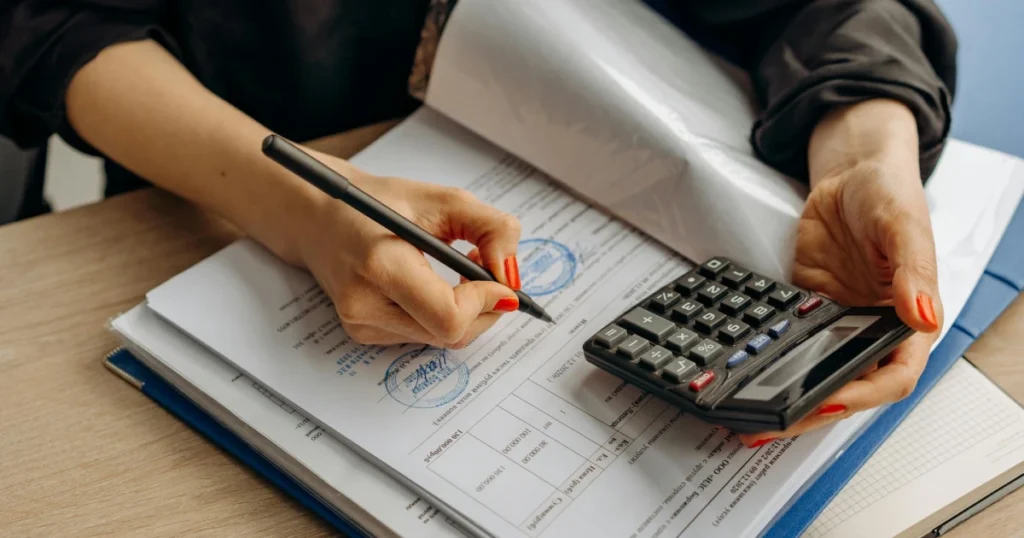 mãos femininas segurando uma calculadora e um lápis em cima de alguns papais para ilustrar o tema revisão da aposentadoria